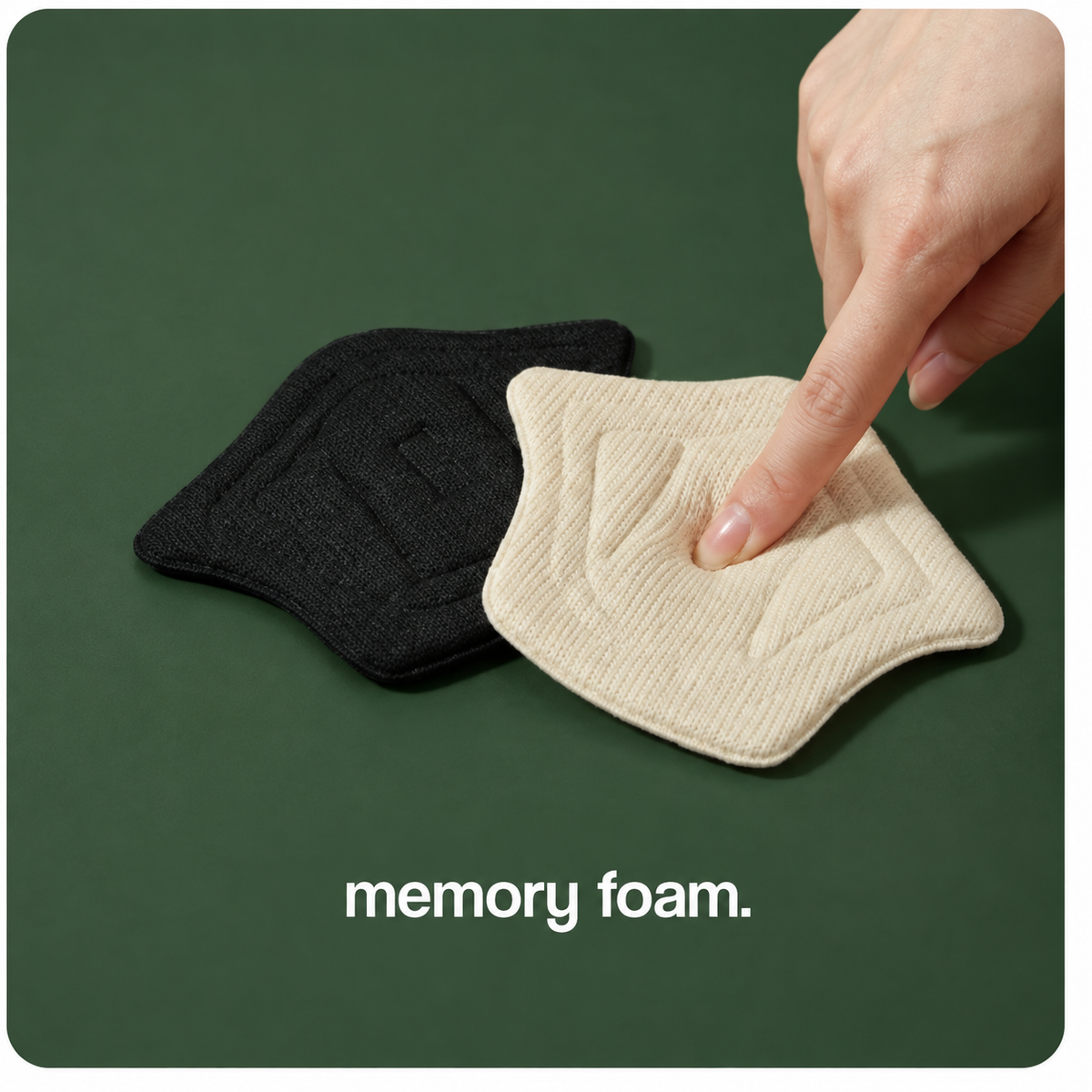 A finger pressing a cream memory-foam heel pad beside a black pad on a forest-green backdrop.
